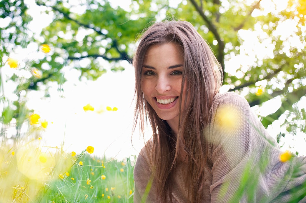 Junge lächelnde Frau, die bei Sonnenschein im Gras liegt.